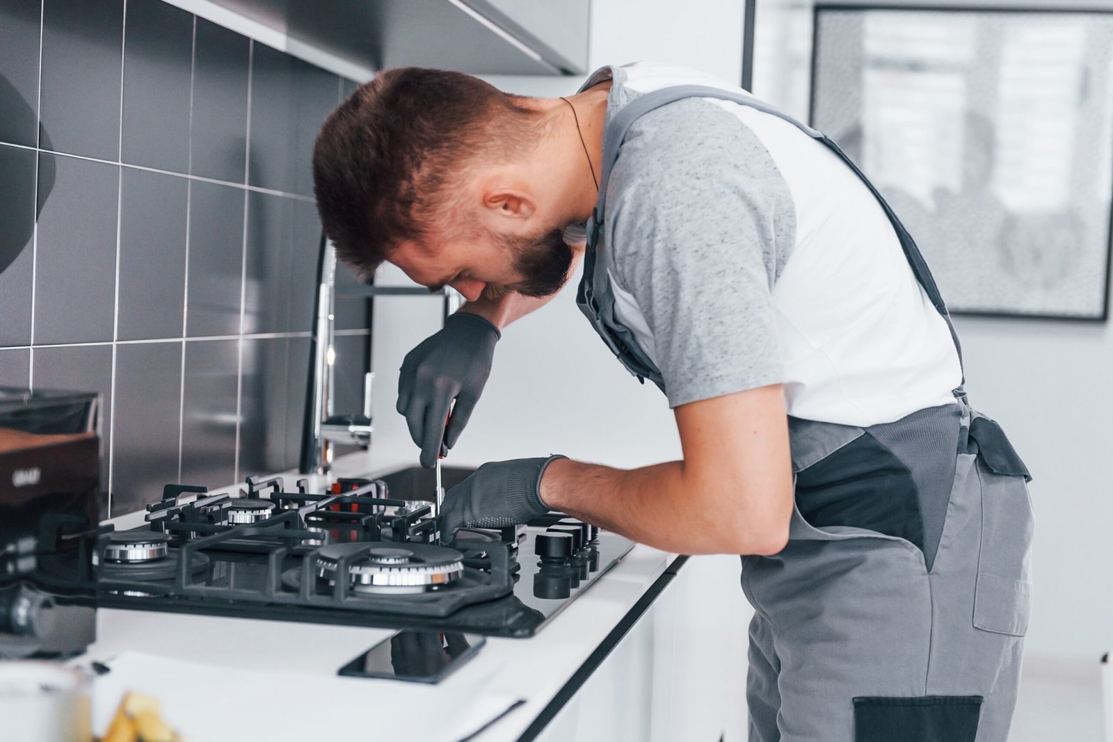 Young professional plumber in grey uniform working on the kitchen.